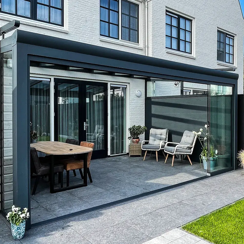 Glazen veranda aan huis met zonwering, uitkijkend op een verzorgde tuin met een stijlvolle tuinset geplaatst door Alu Solution